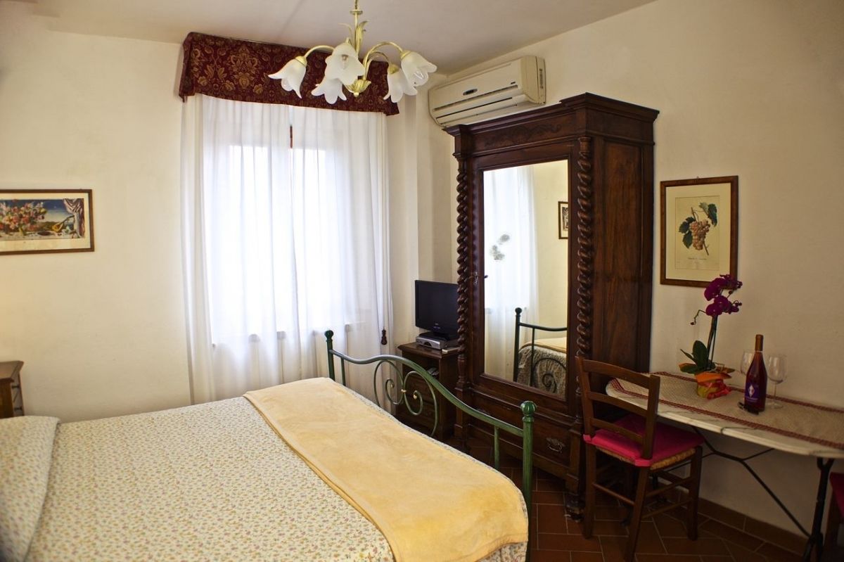 A bedroom with a bed, a desk with a chair, a mirror, and a window with curtains.