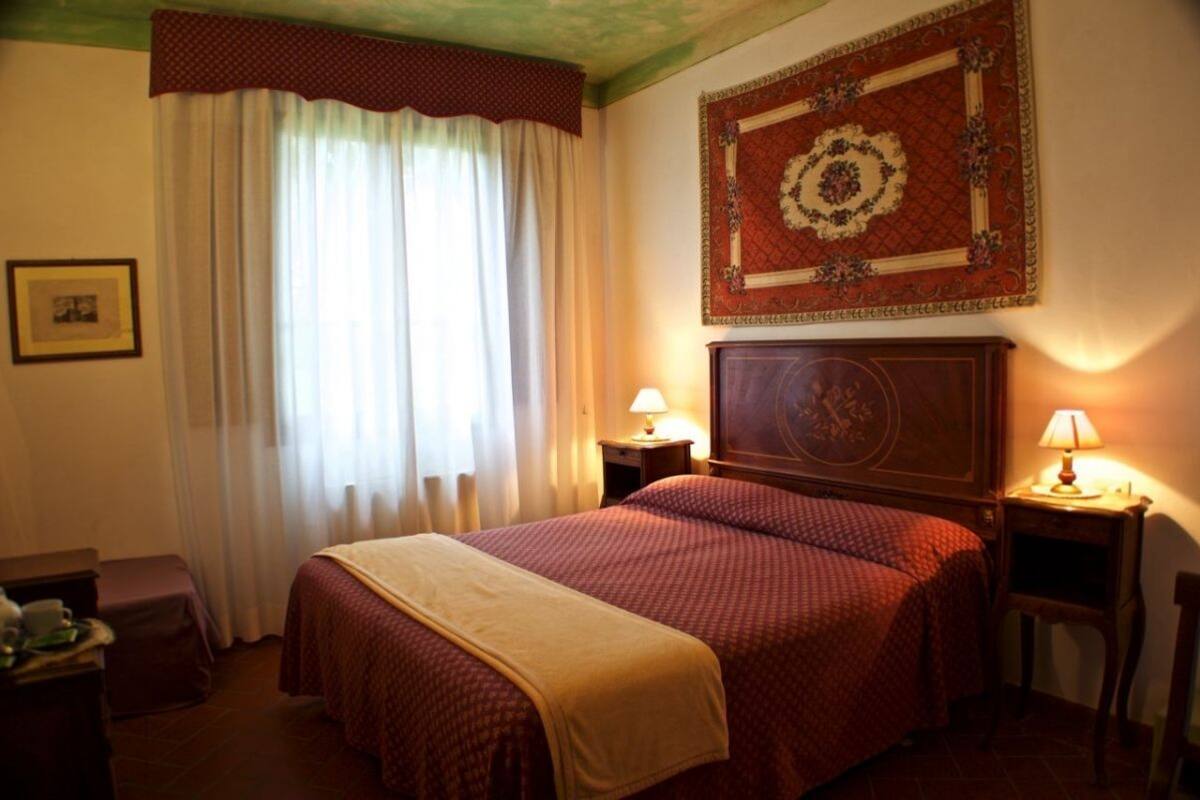 A hotel room with a large bed, two bedside tables with lamps, a framed artwork above the bed, and a window with curtains.