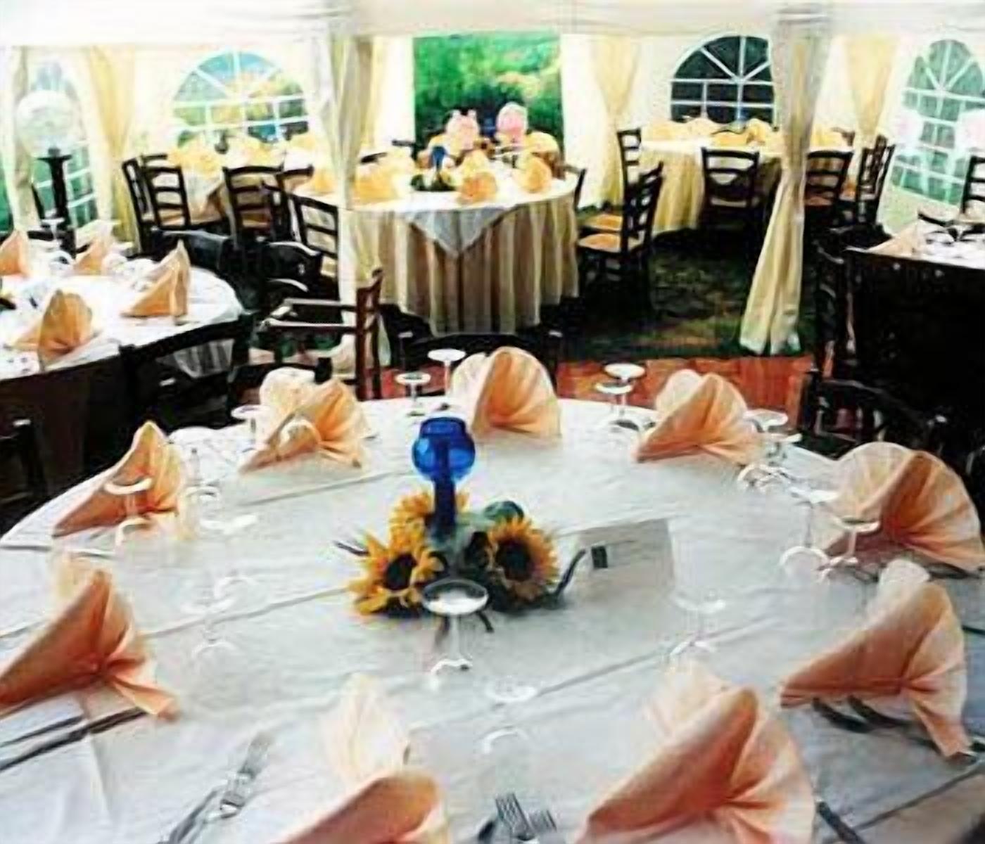 Un salón de banquetes con mesas redondas dispuestas para un evento formal, con manteles blancos, servilletas color melocotón y centros de mesa florales.