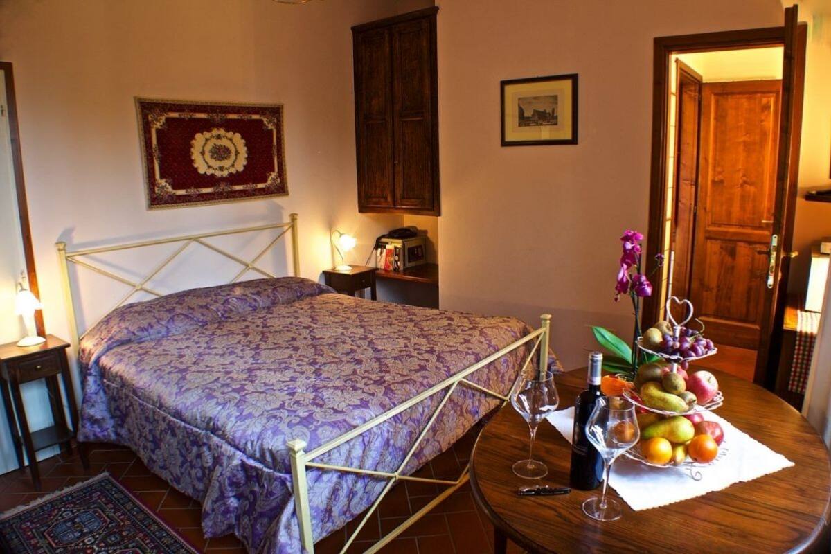 A bedroom with a bed, bedside table, lamp, and a fruit and wine basket on a round table.