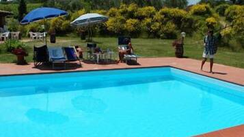 A swimming pool with lounge chairs and umbrellas, surrounded by greenery.