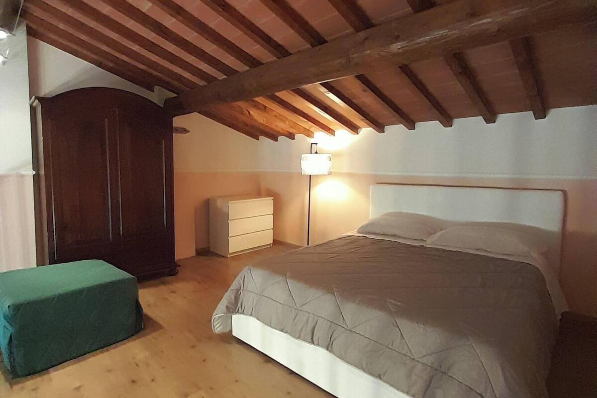 A bedroom with a wooden ceiling, a bed with a white headboard, a bedside lamp, and a green bench.