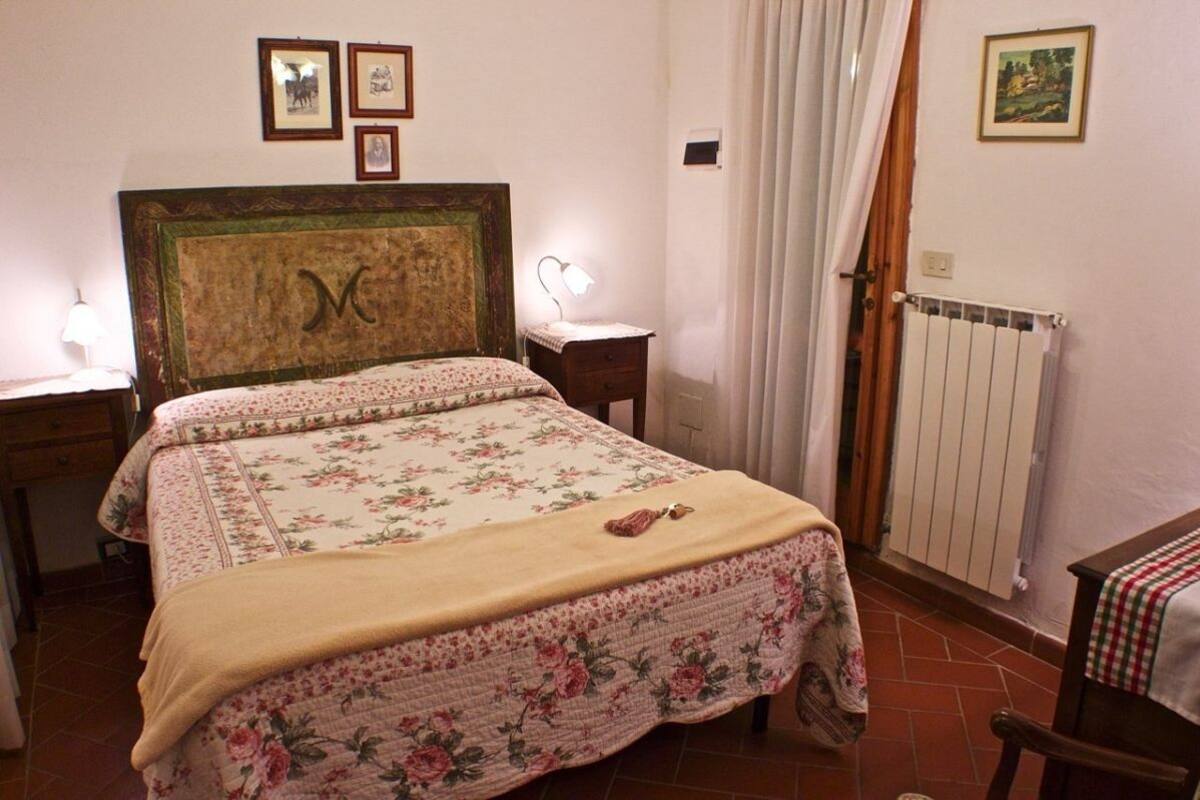 A bedroom with a bed, a bedside table, a lamp, a radiator, and a window with curtains.