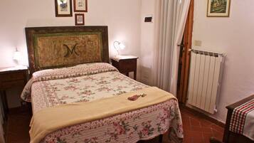 A bedroom with a bed, a bedside table, a lamp, a radiator, and a window with curtains.