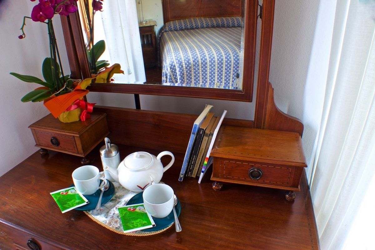 Een houten dressoir met spiegel, een klein nachtkastje, een bed met gestreept beddegoed en een potorkidee.