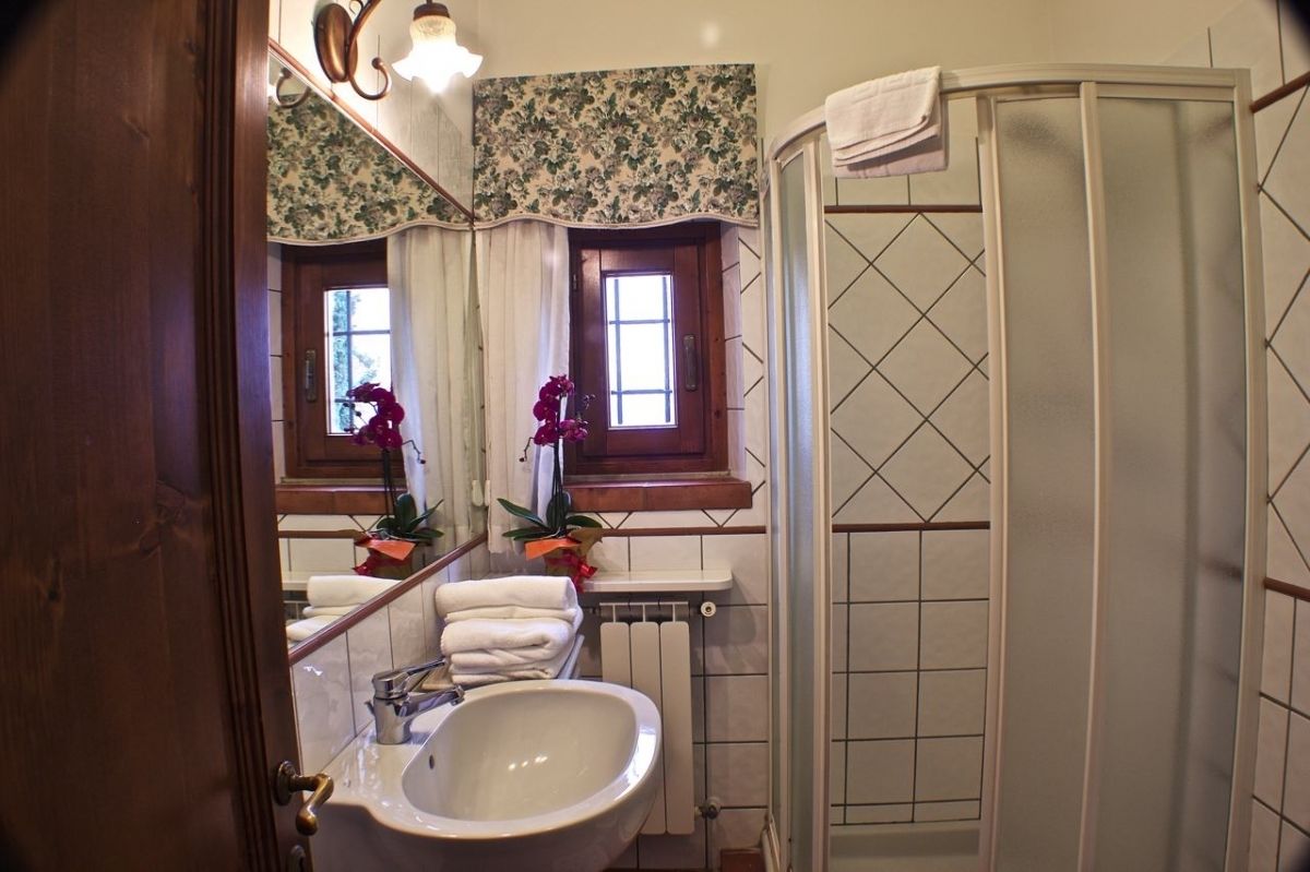 Un baño con un lavamanos blanco, un espejo, una ducha y una ventana con papel tapiz floral.