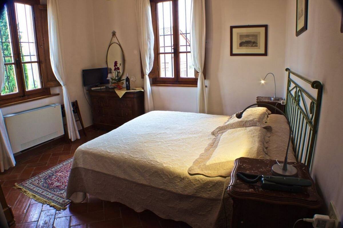A neatly arranged bedroom with a bed, bedside tables, a dresser, a window with curtains, and a radiator.
