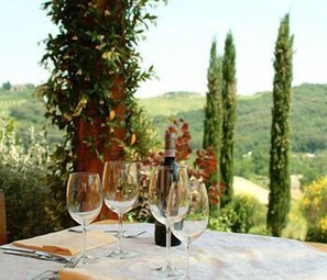 Une table avec trois verres à vin et une bouteille, le tout placé devant un paysage de vignoble et de collines ondoyantes.