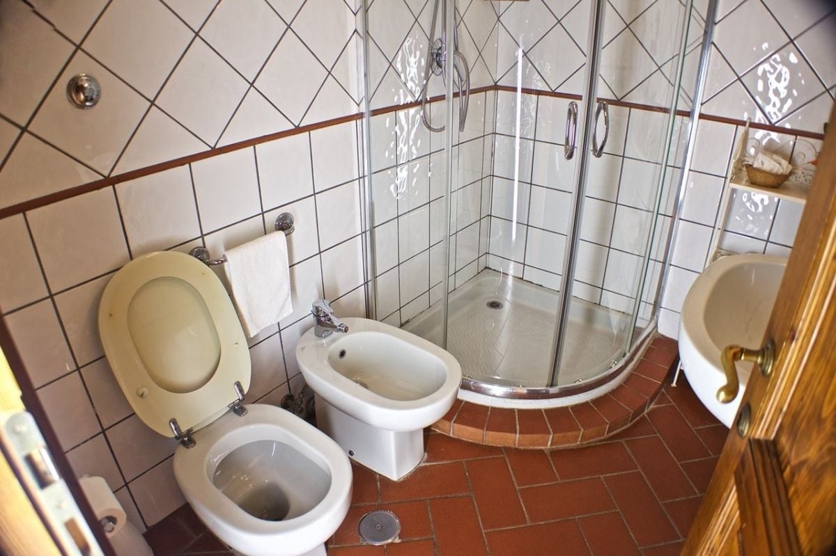 Un baño con inodoro, bidé y cabina de ducha con mampara de vidrio.
