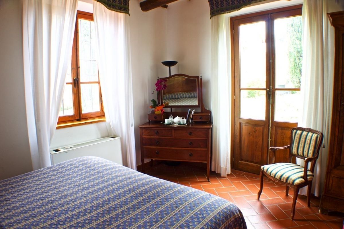 A bedroom with a bed, a wooden dresser, a chair, and a large window.