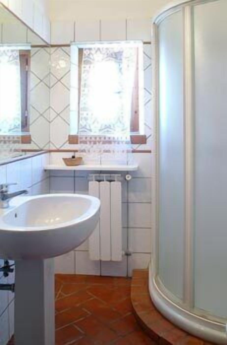 Un baño con lavamanos blanco, un espejo, una ventana con vistas y una zona de ducha.