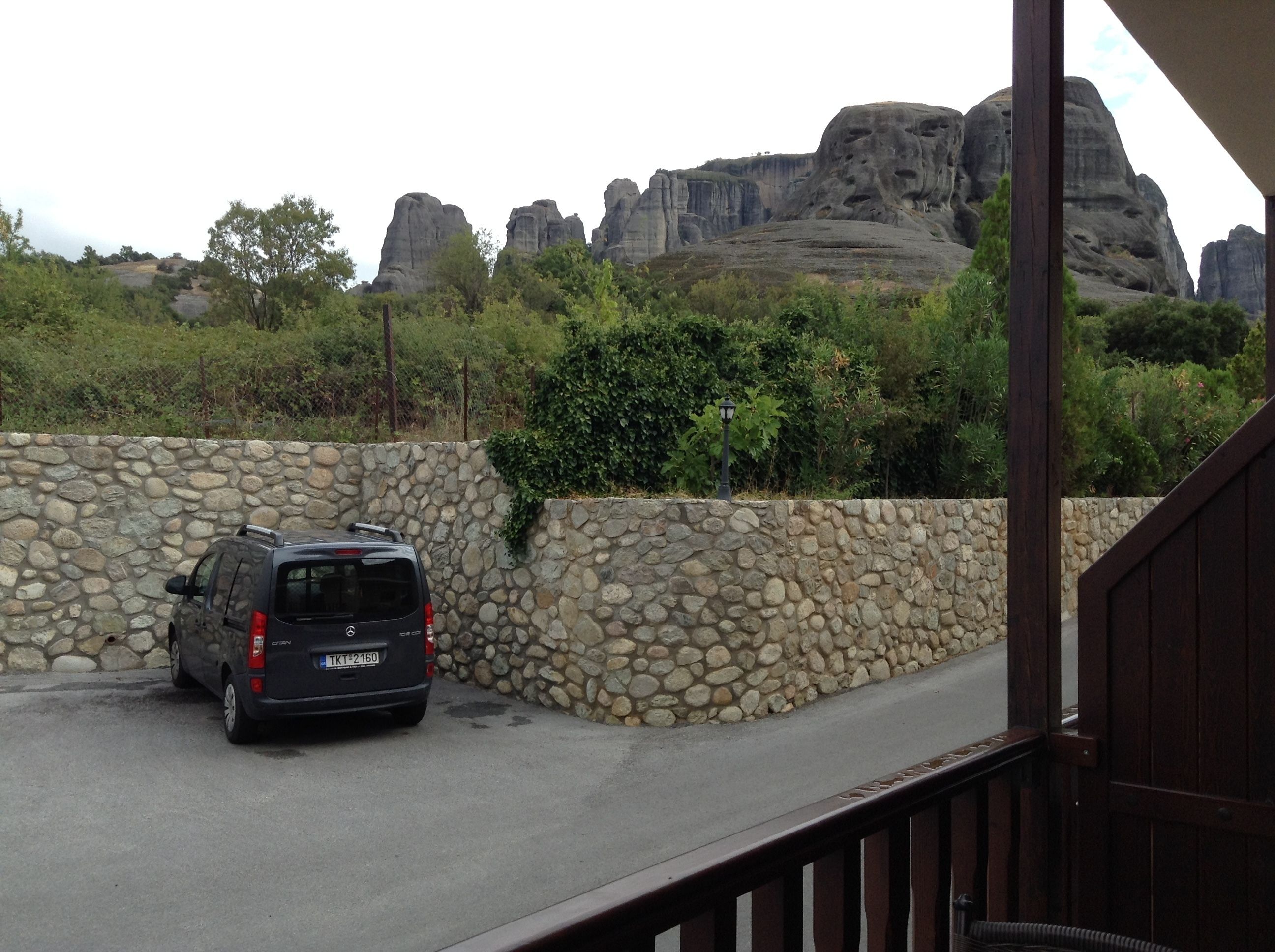 A car parked beside a stone wall with a view of rocky formations in the background.