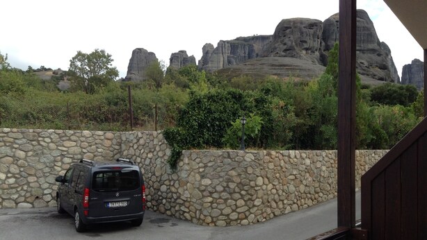 A car parked beside a stone wall with a view of rocky formations in the background.
