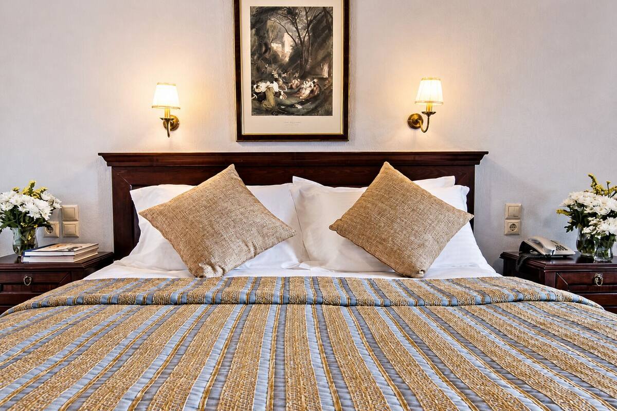 Ein Hotelzimmer mit einem großen Bett, zwei Wandlampen, einem gerahmten Kunstwerk über dem Bett und einem Nachttisch mit Telefon und Blumen.