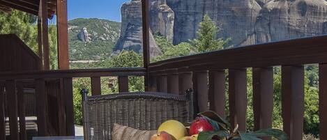 A balcony with a table, a wicker chair, and a view of a mountain.