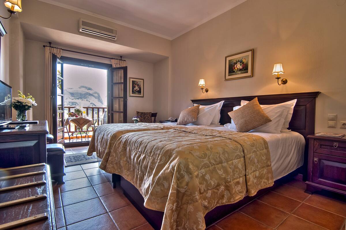 Ein Hotelzimmer mit einem großen Bett, einem Schreibtisch mit Stuhl, Blick auf die Berge durch eine geöffnete Tür und zwei Wandlampen.