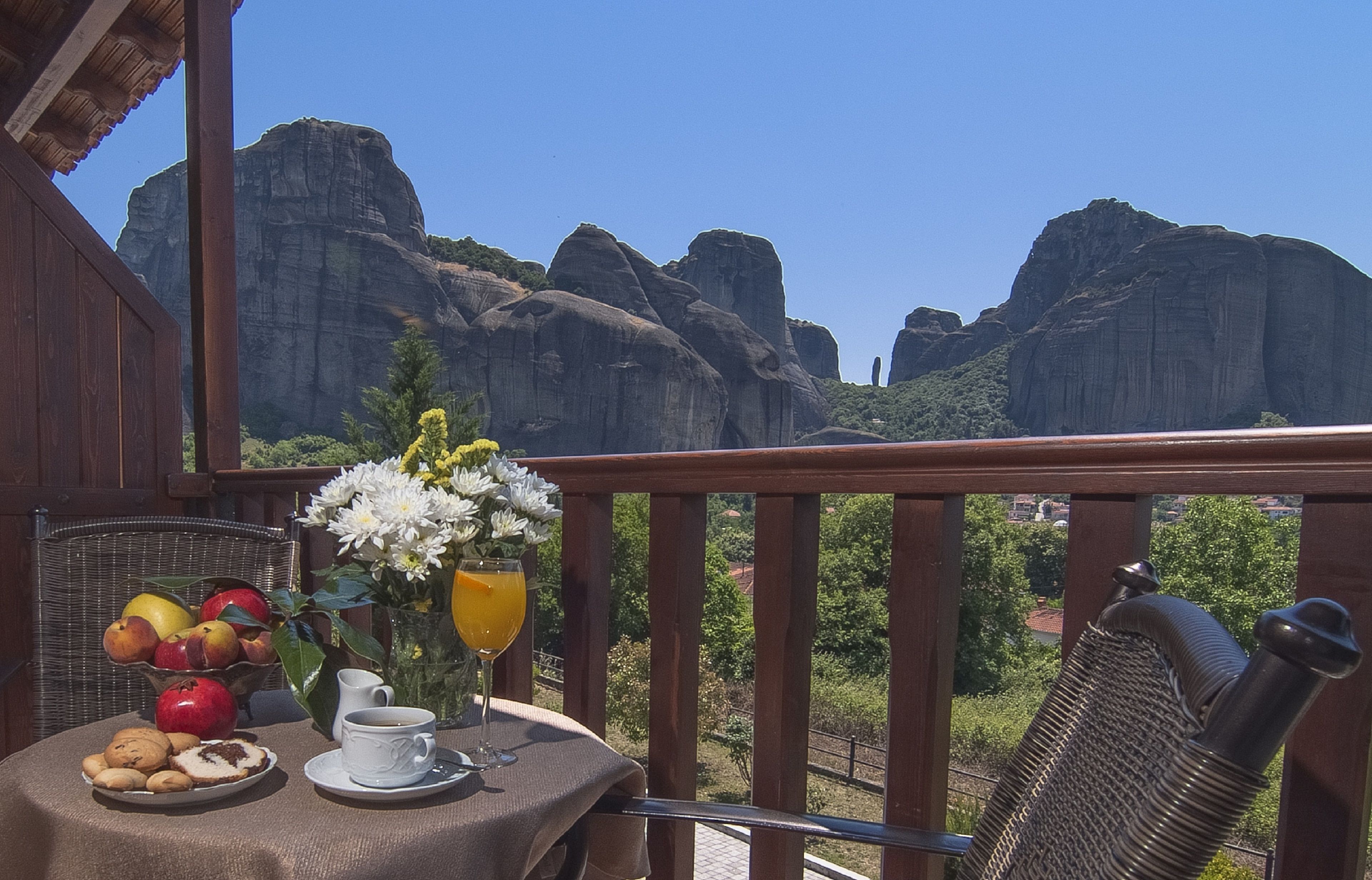 Un balcón con una mesa dispuesta para el desayuno, que incluye frutas, galletas y bebidas, con vistas a un paisaje montañoso.