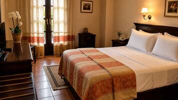 Een hotelkamer met een bed, bureau, stoel, een kamerplant, een deur en een raam met gordijnen.