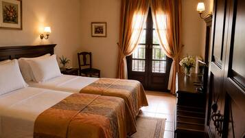 A hotel room with two beds, a desk, a chair, an air conditioning unit, and a view through a door.