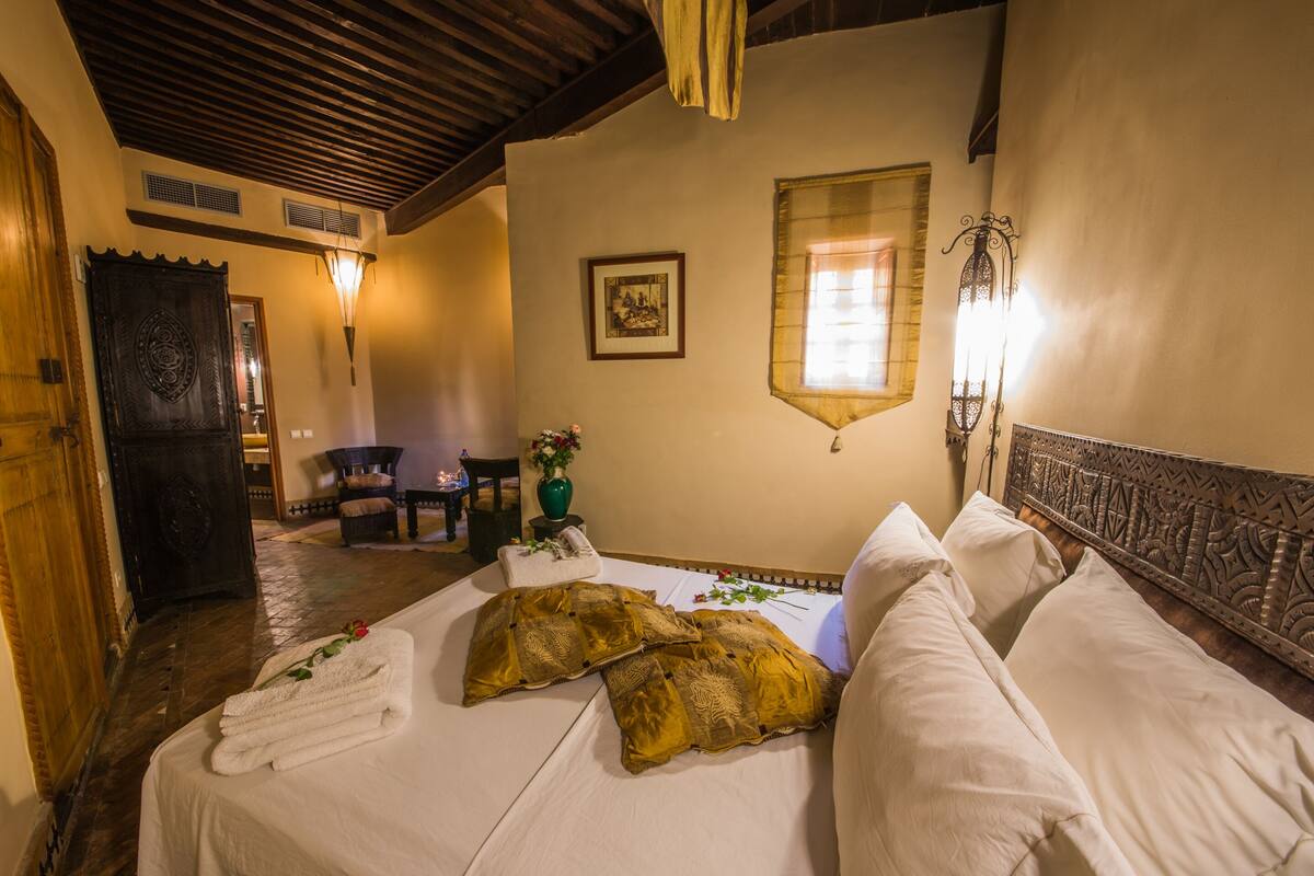 Une chambre d’hôtel avec un lit, une porte en bois, une petite table avec un vase et un tableau accroché au mur.
