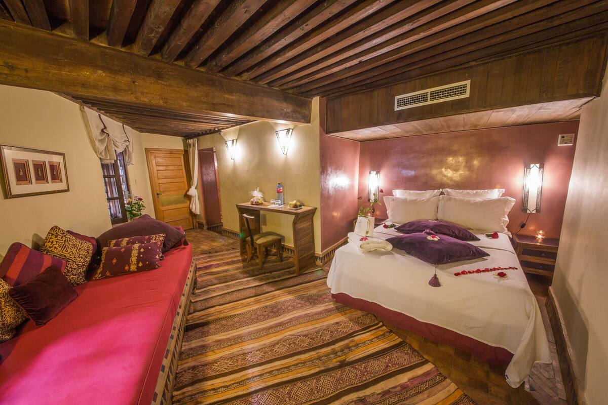 Une chambre d’hôtel avec un grand lit, un canapé rouge, un plafond en bois et une moquette à motifs.