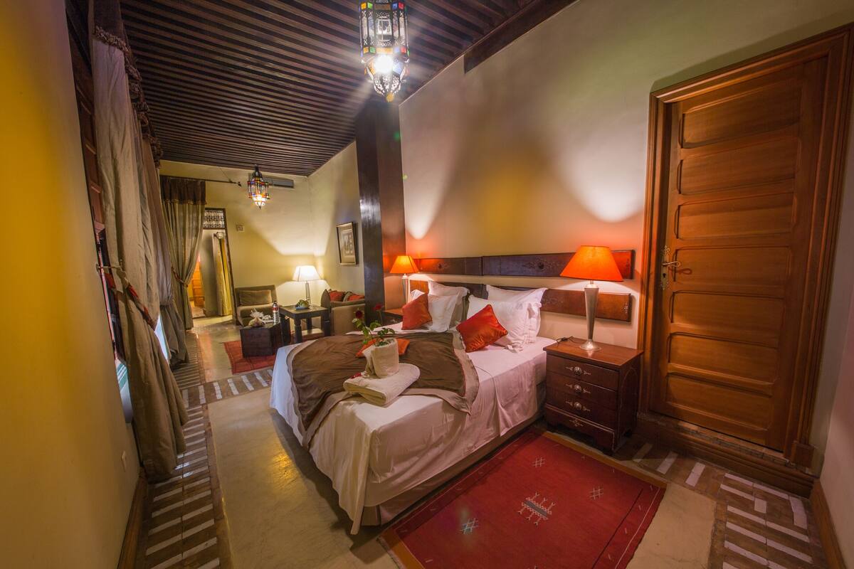 Une chambre d’hôtel avec un lit, des tables de chevet, une porte en bois et un tapis rouge.