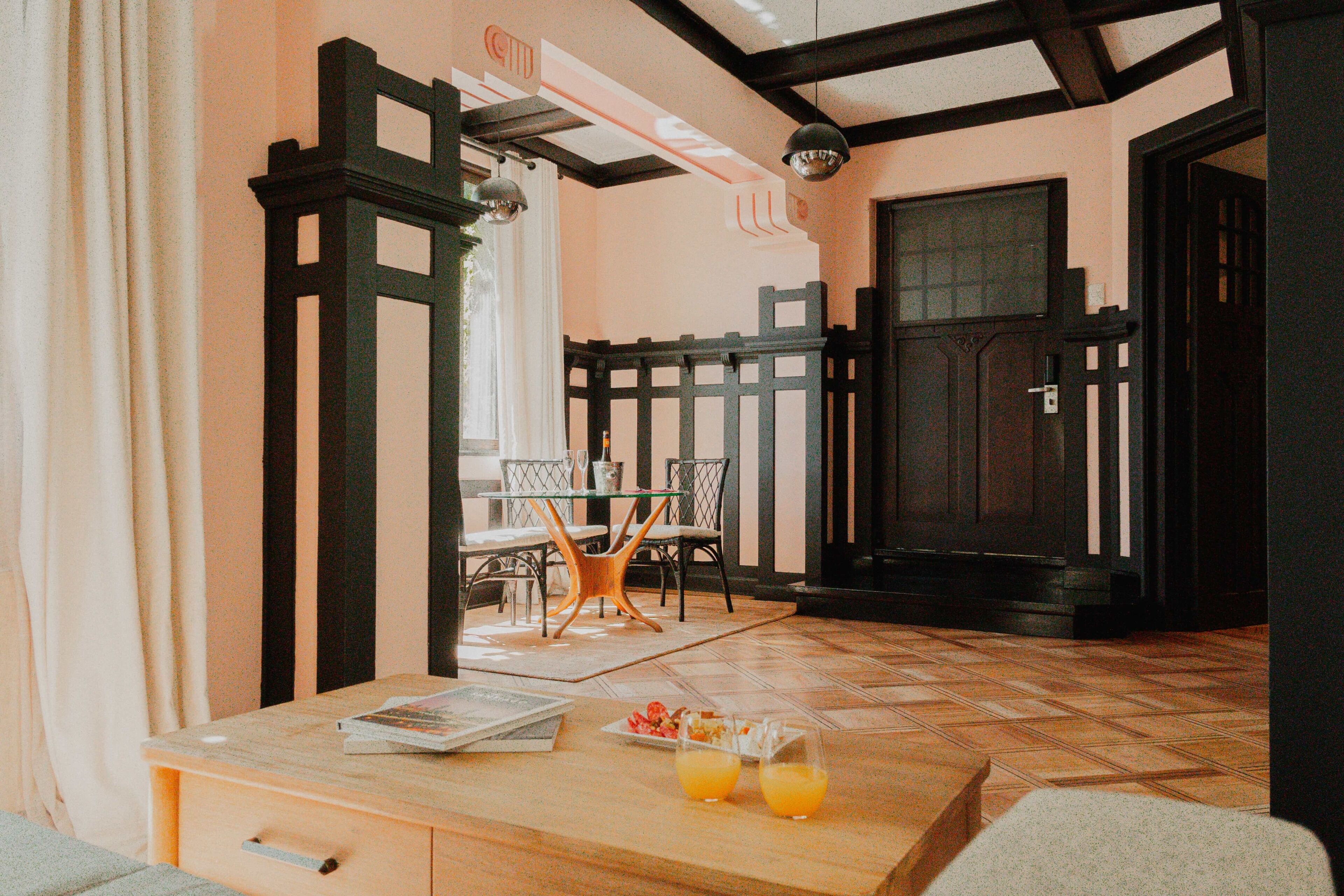 A room with a wooden table, two chairs, a dining table with chairs, and a black door.