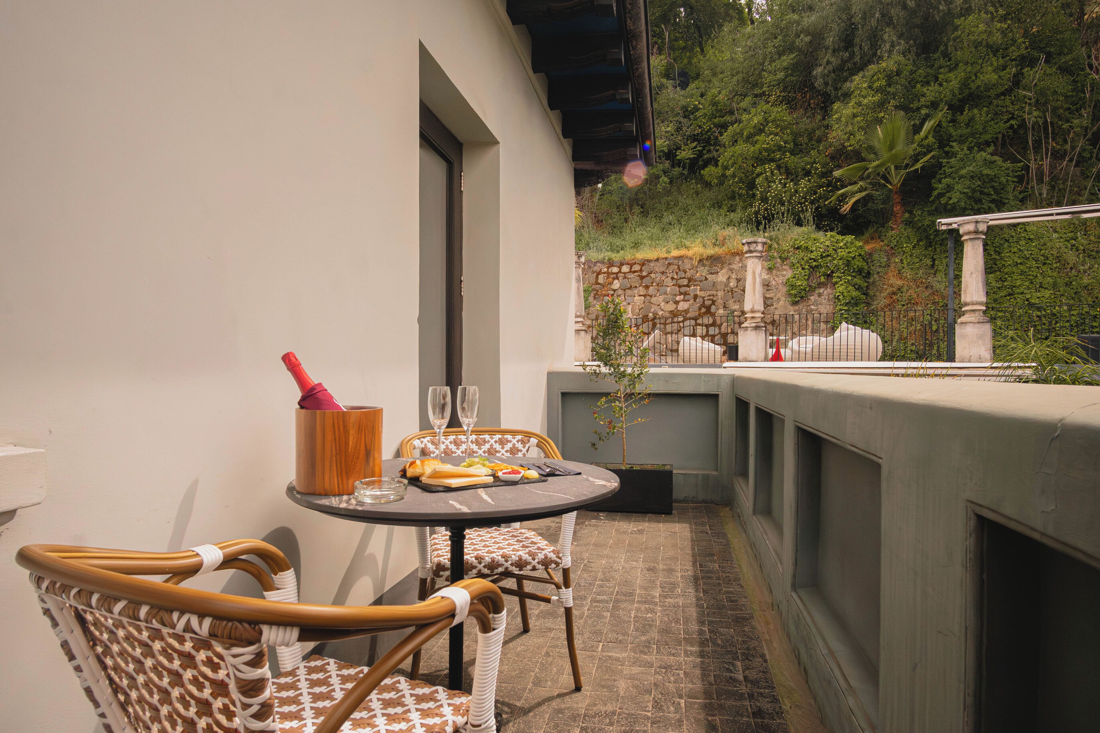 A patio with a round table, two chairs, a wine bottle, and a fruit bowl.