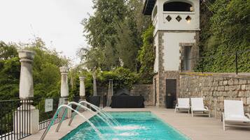 Ein Swimmingpool mit Wasserfall, Liegestühlen und einer Steinwand, die mit Grünpflanzen bewachsen ist.