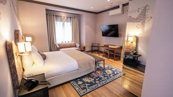 A hotel room with a bed, bedside table, lamp, TV, desk, chair, and a decorative mirror.