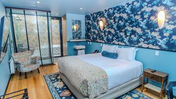A bedroom with a large bed, a chair, a small table, a mirror, and a wall with a floral pattern.