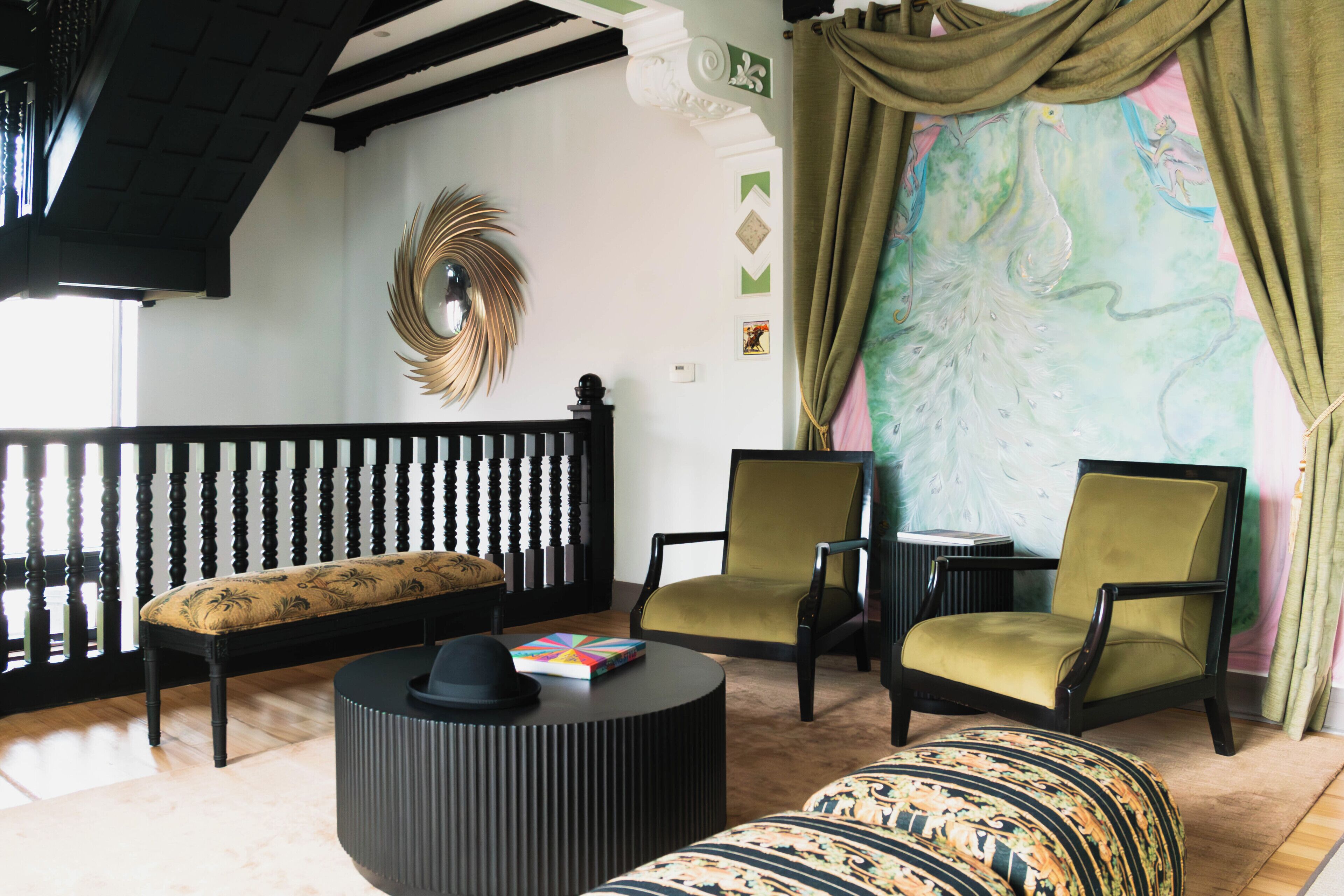 Een kamer met een zwart-wit gestreepte bank, twee groene fauteuils, een rond zwart pouf en een decoratieve spiegel aan de muur.