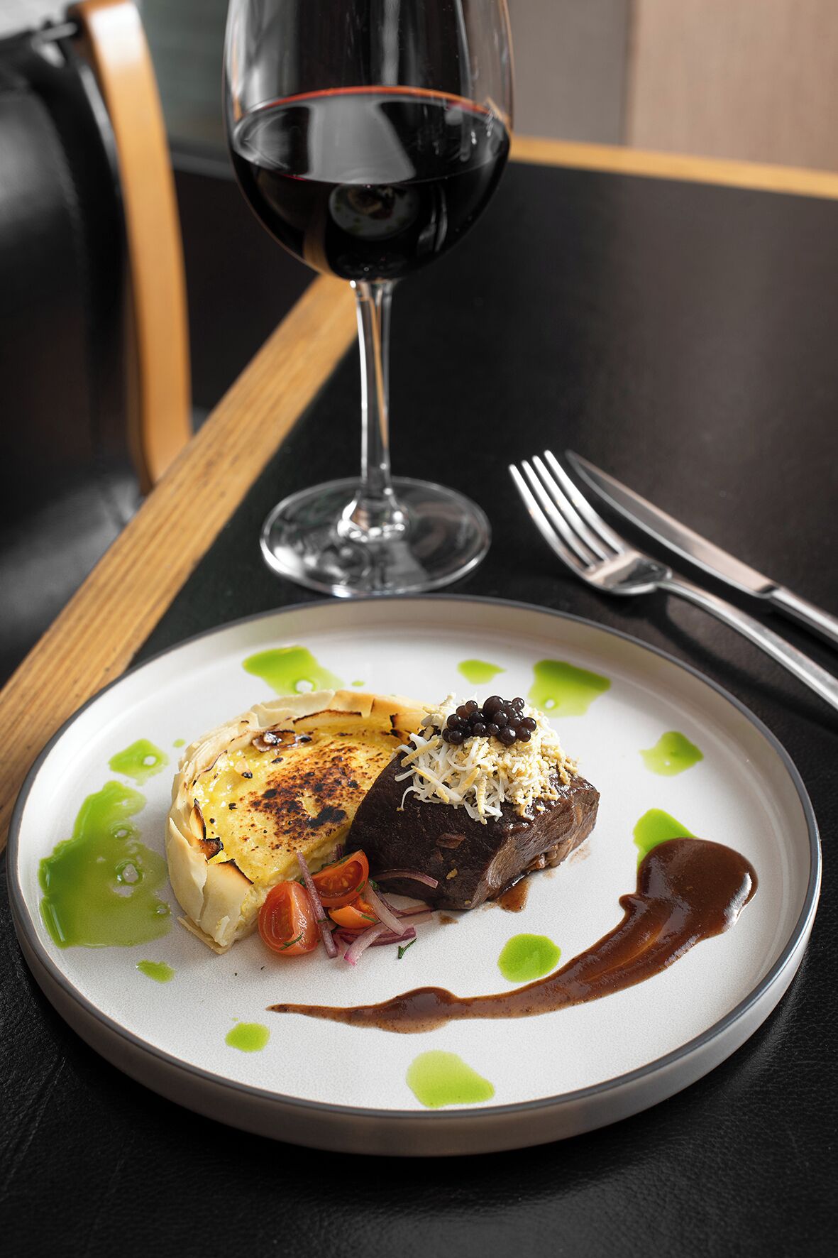 Une assiette de nourriture accompagnée d’un verre de vin rouge, posée sur une table.