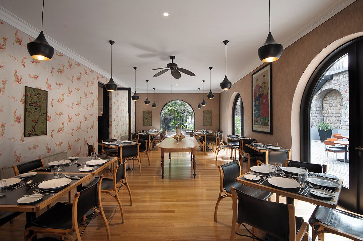 A restaurant with wooden tables, black chairs, and hanging pendant lights.