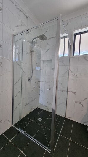 A glass-enclosed shower with a handheld showerhead, a control panel, and a black tiled floor. - Seaview Motel and Apartments (Apollo Bay)