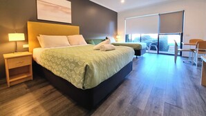 A modern hotel room with a large bed, a desk, and a balcony with a view. - Seaview Motel and Apartments (Apollo Bay)