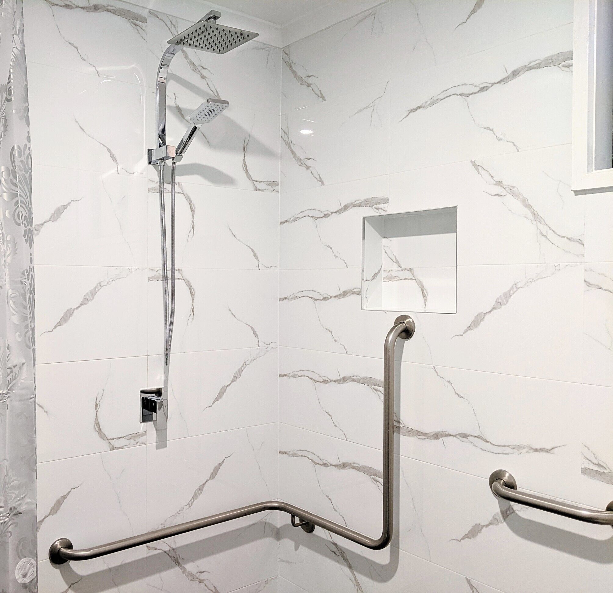 A bathroom with white marble tiles, a shower with a handheld showerhead, and grab bars for accessibility.