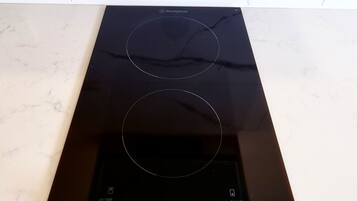 A black induction cooktop with two knobs and a control panel on a white marble countertop.