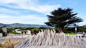 A wooden fence with a tree in the center, a building with a curved roof, and a parking area with cars.