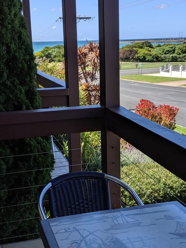 A balcony with a wicker chair, a view of the ocean, and a road in the background.