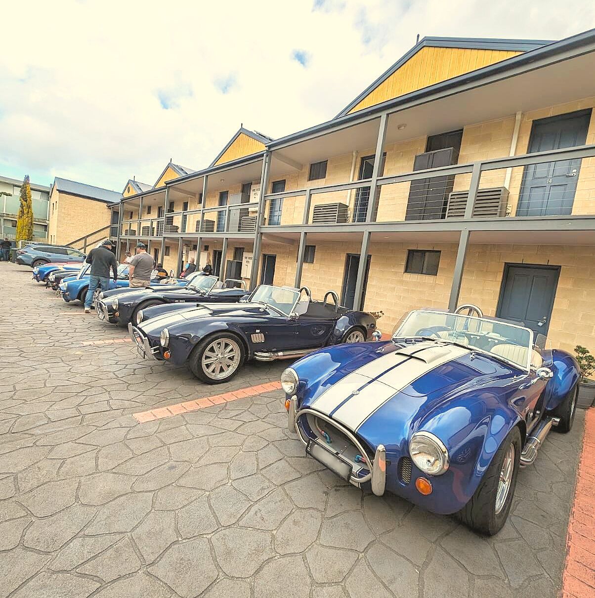 A row of classic cars parked in front of a building with balconies.