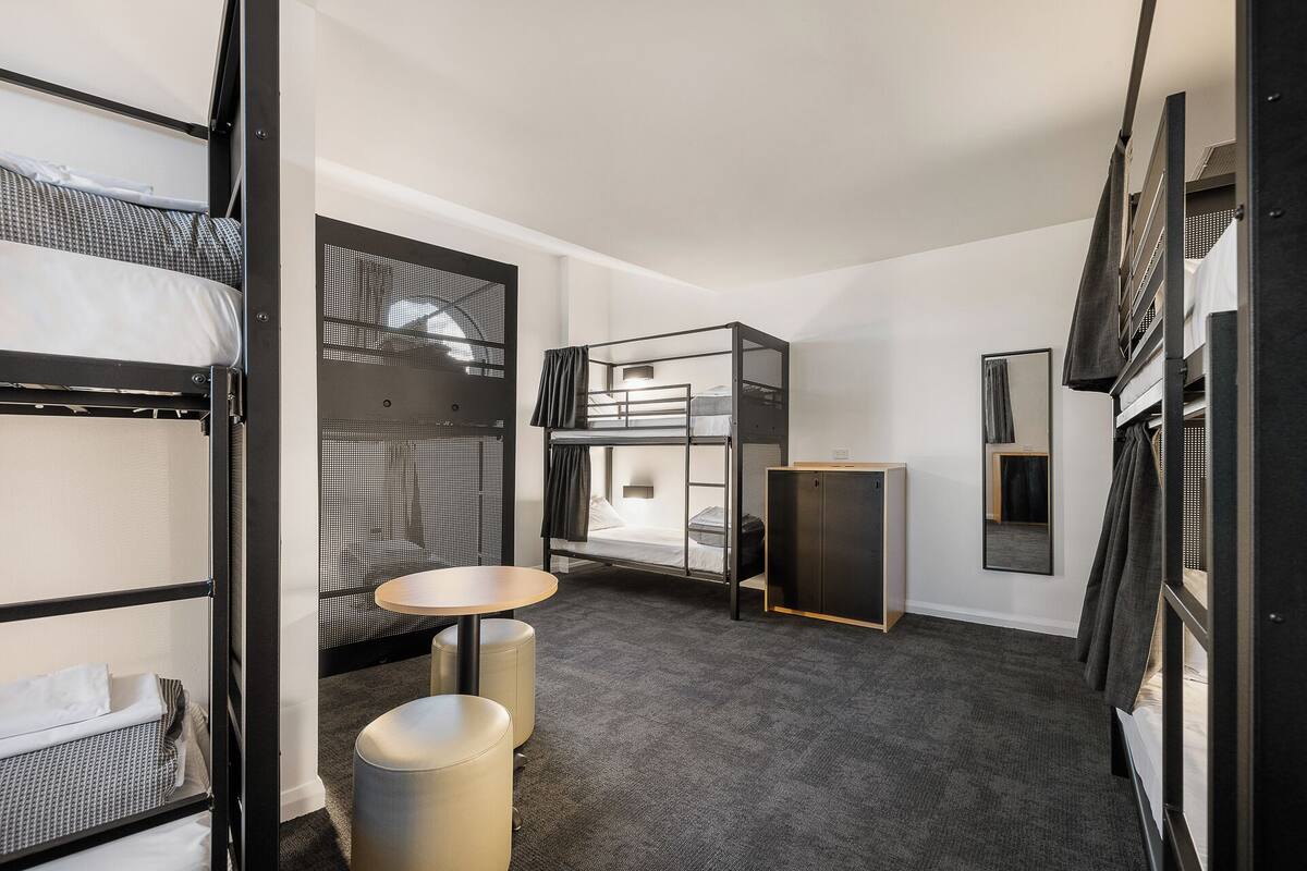 Habitación de hotel compacta con literas, una mesita redonda y un espejo.