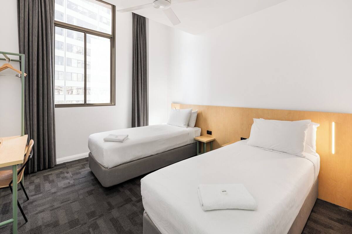 Habitación de hotel con dos camas, un escritorio y una ventana con cortinas.