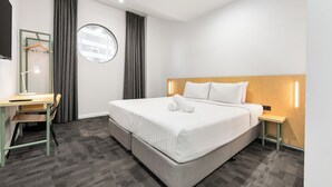 A hotel room with a bed, a desk, a chair, a round mirror, and a nightstand. - YHA Sydney Central (Haymarket)
