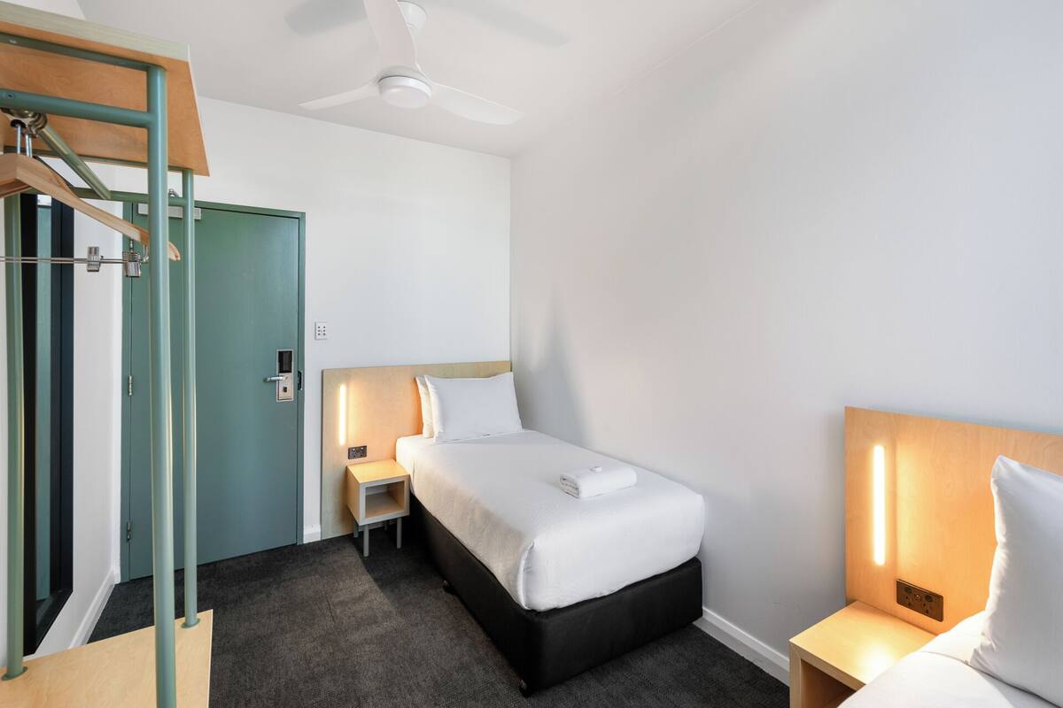 Una habitación de hotel con cama, mesitas de noche, ventilador de techo y una puerta.