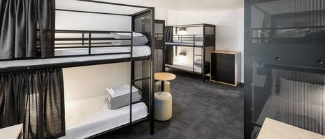 Une chambre d’hôtel moderne et compacte, équipée de lits superposés, d’une petite table ronde et d’un meuble de rangement.