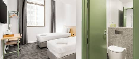 Habitación de hotel con escritorio, dos camas, ventilador de techo y baño con inodoro y lavamanos.