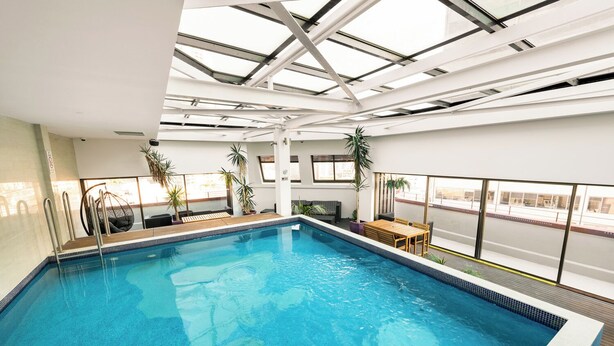 An indoor swimming pool with a glass ceiling, surrounded by seating and potted plants. - YHA Sydney Central (Haymarket)