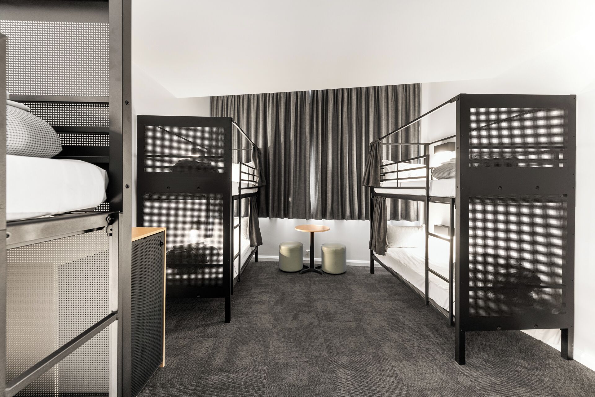 A modern hotel room with bunk beds, a small round table, and a view of the city through the window.