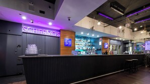 A bar area with a neon sign, shelves with bottles, and a counter with glasses. - YHA Sydney Central (Haymarket)
